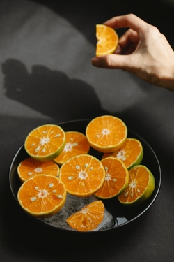 From above crop anonymous person demonstrating slice of fresh ripe orange under bowl with delicious fruits with melting ice